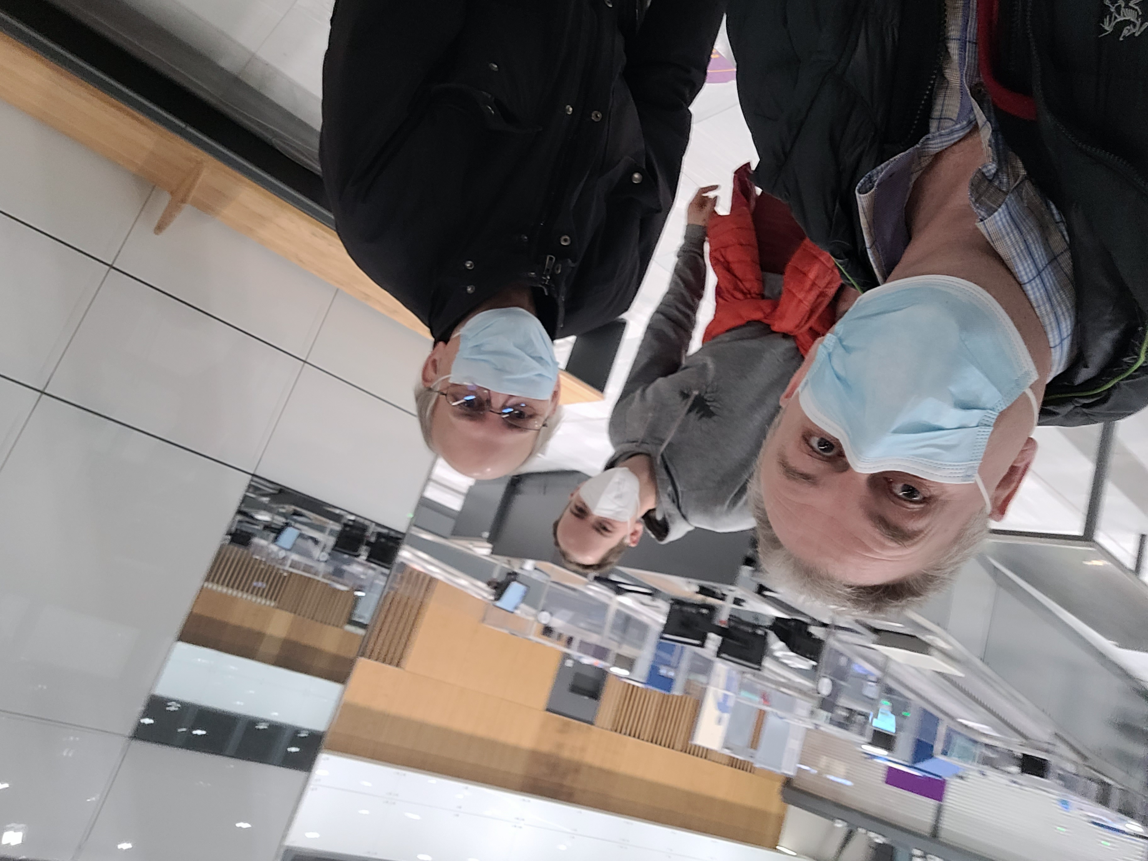 Tre personer med ansiktsmaske ser i kamera på flyplass