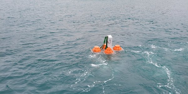 

Grå metallboks med oransje flyteelementer på hver side flytende i sjøen.