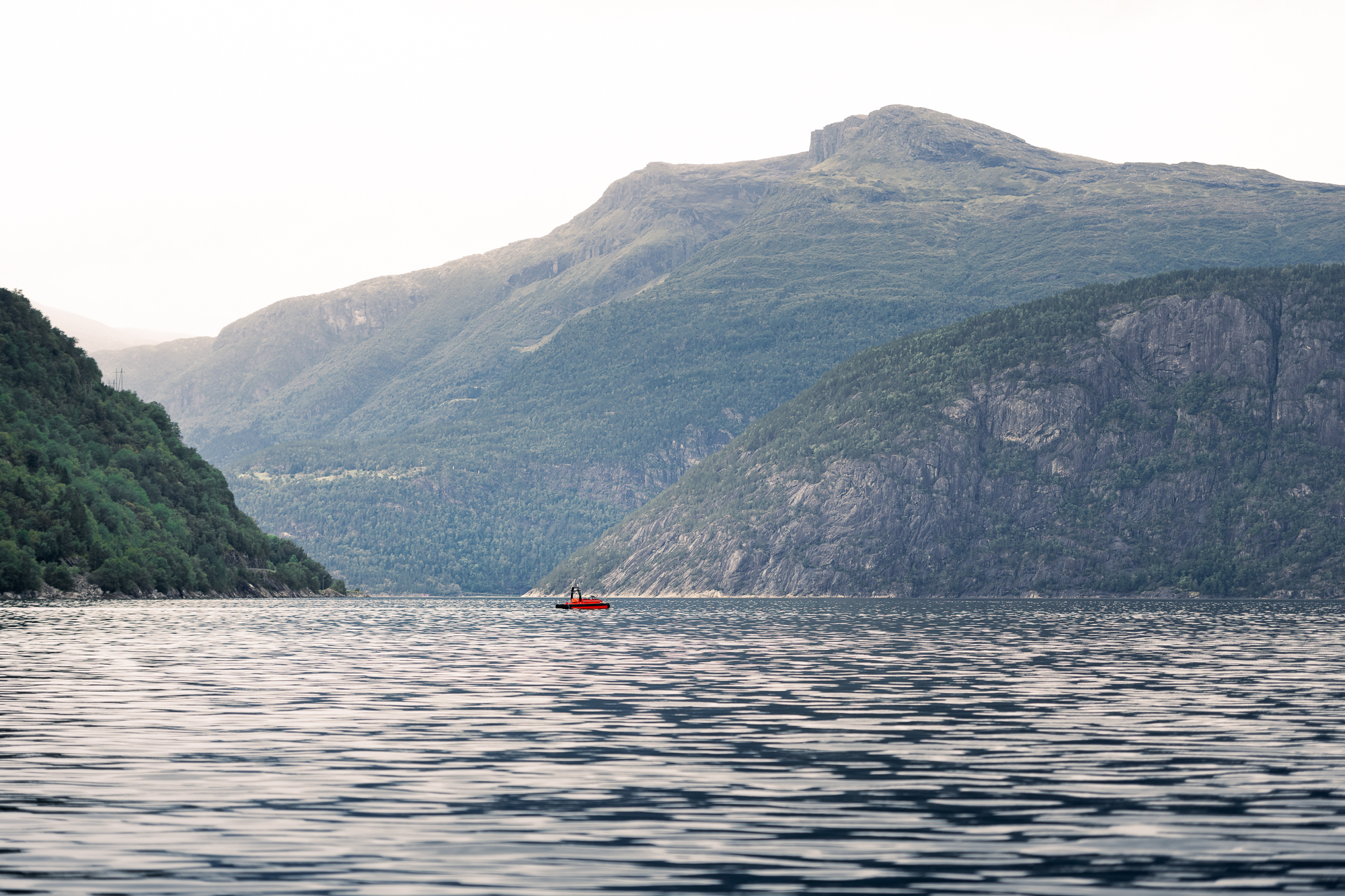 Liten oransje båt på fjord med fjell rundt