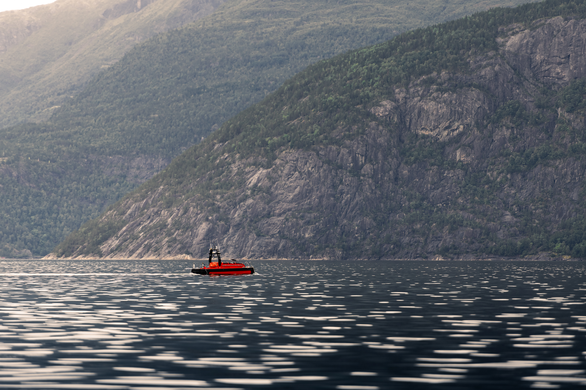 Oransje fartøy ute på fjord med bratte fjellsider rundt.