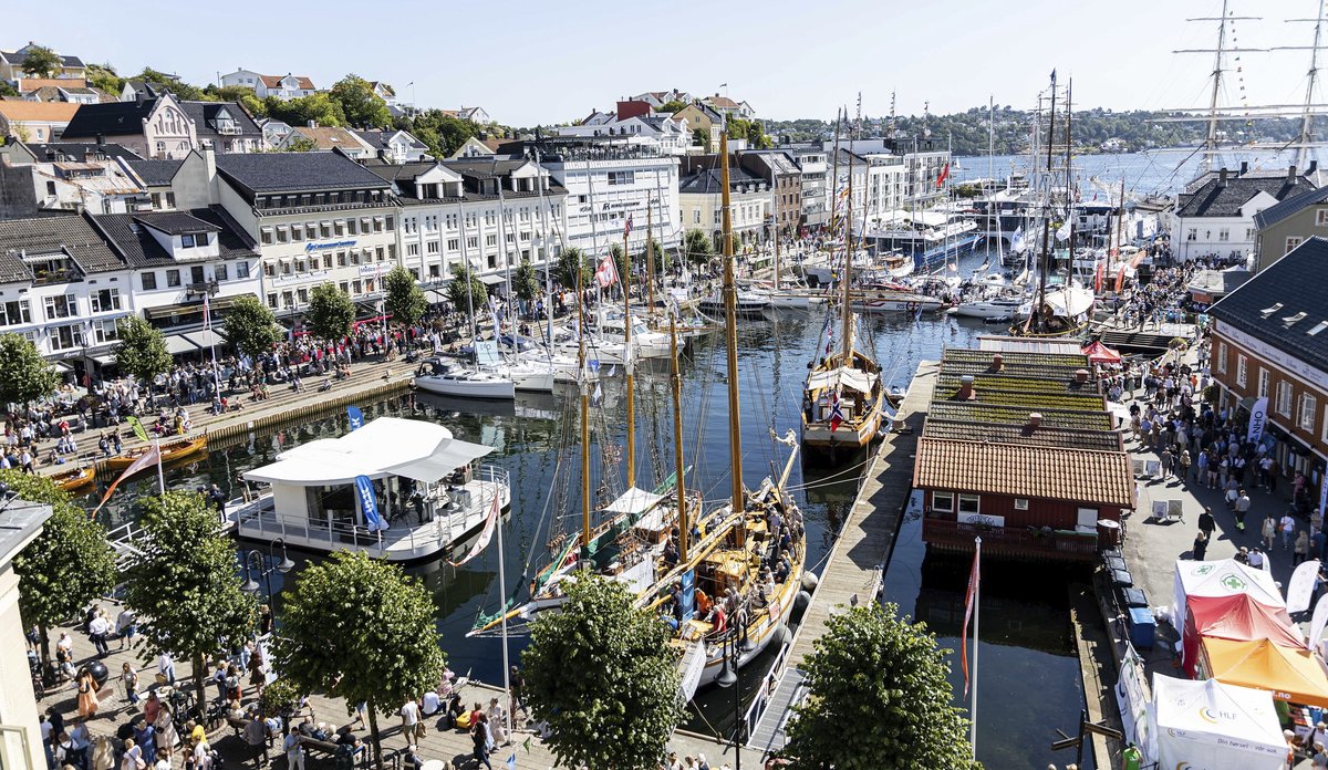 Havn med seilbåter, seilskuter og masse folk på land.