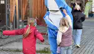 To jenter hilser på noen som er utkledd som hai. Haikostymet er blått og hvitt. 