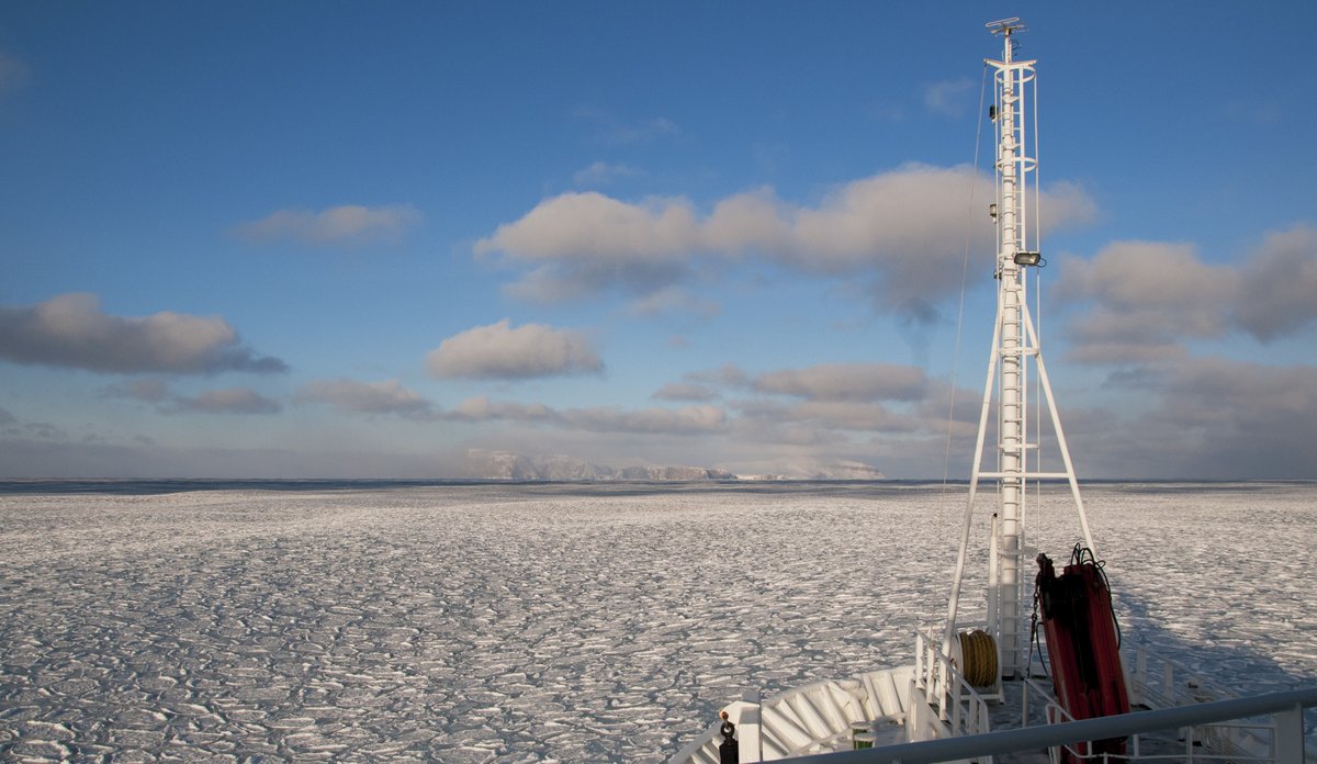 The bow of a ship in the foreground and white sea ice in the background.