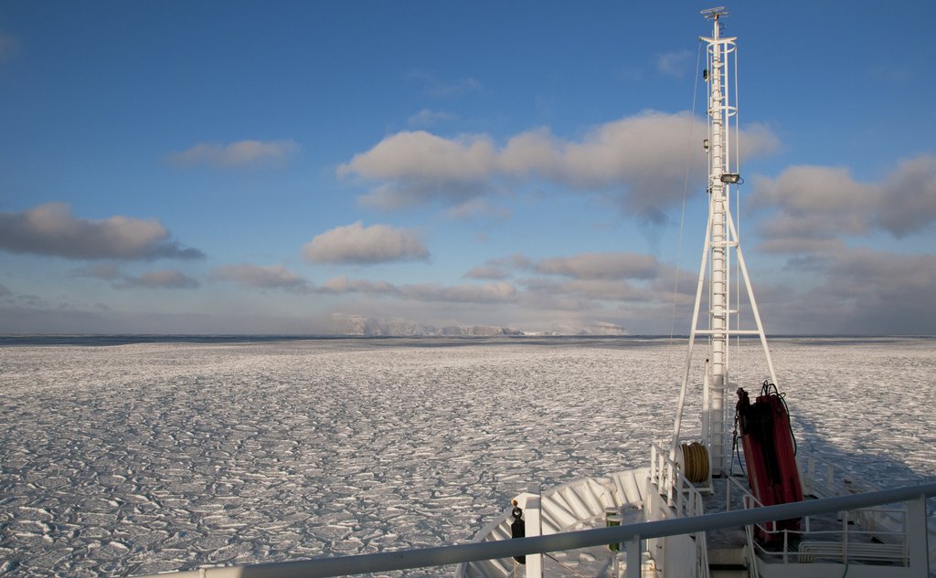 The bow of a ship in the foreground and white sea ice in the background.