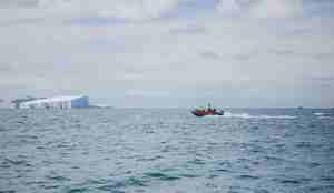 lettbåt i full fart gjennom havet med isfjell i bakgrunnen