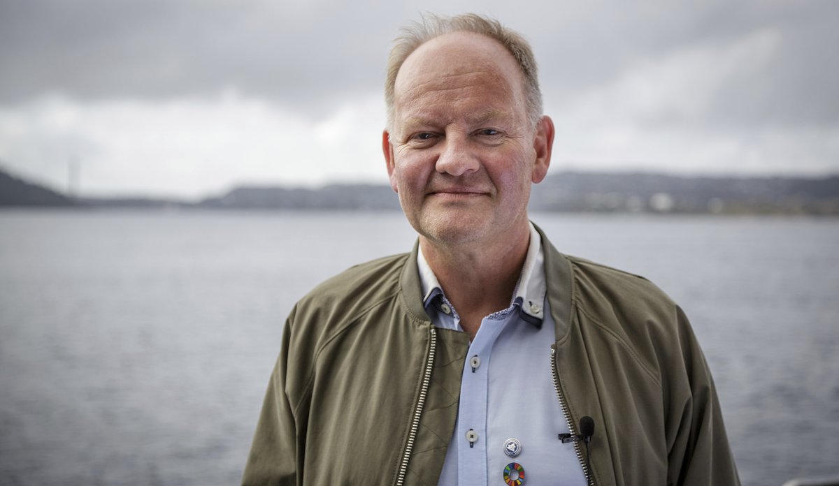 En mann ser mot kameraet. Bak han ser en fjord og horisont møtes