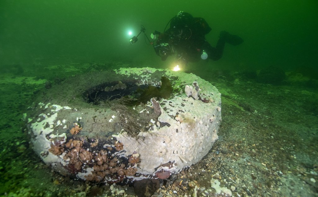 Stort dekk på havbunnen dekket av hvitt havnespy og med dykker i bakgrunnen