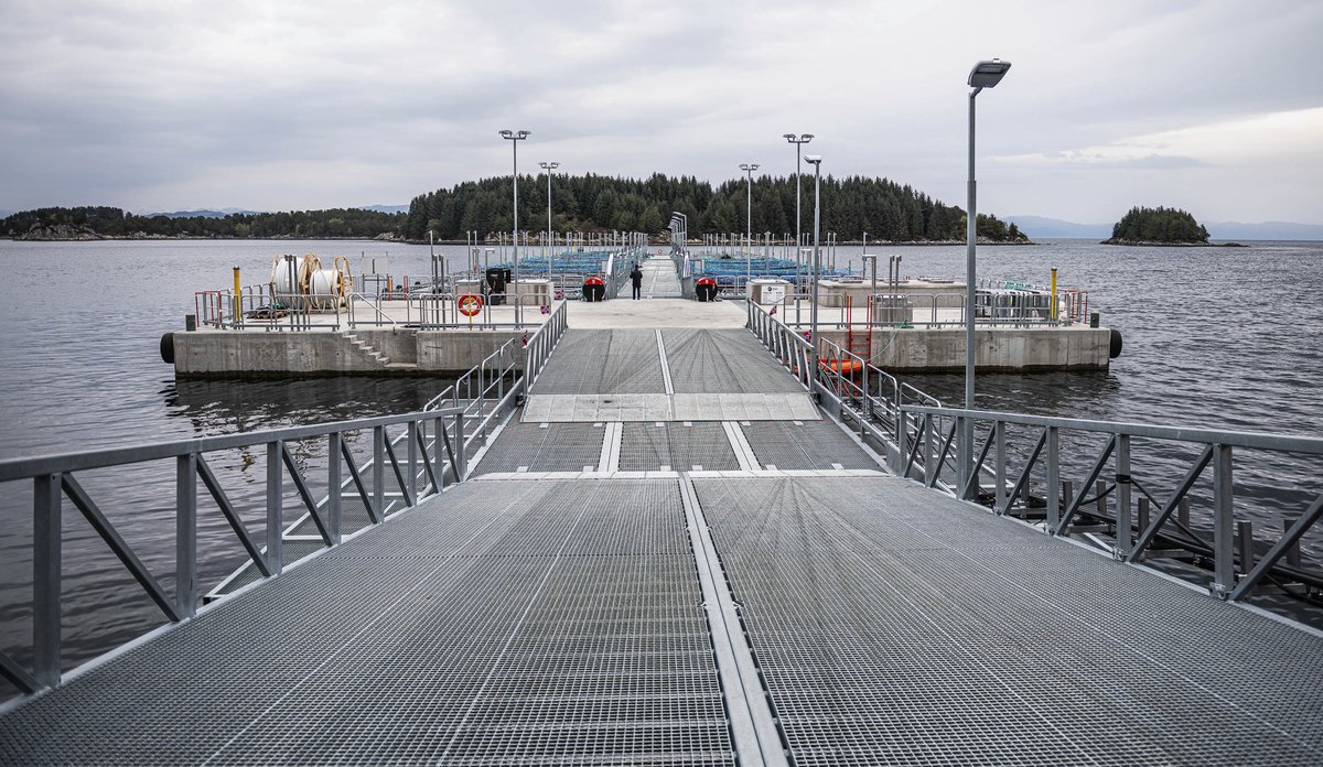 Landgang mot en betongplatting og flere fiskemerder i bakgrunnen.