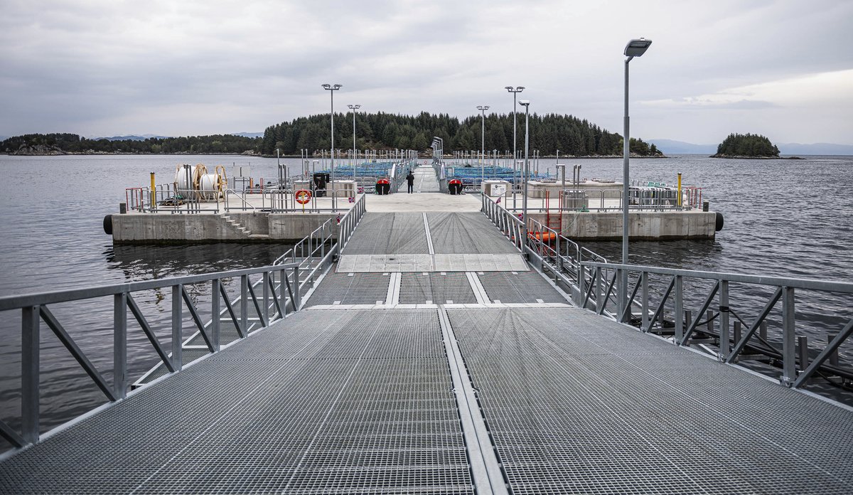 
Landgang mot en betongplatting og flere fiskemerder i bakgrunnen.