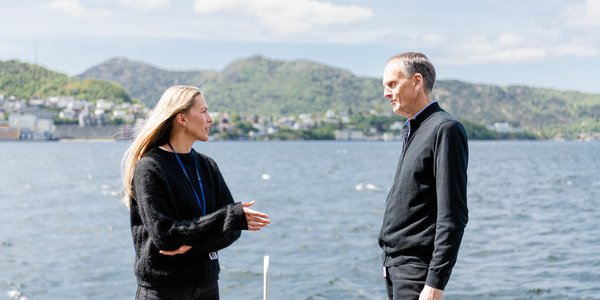 

Peter Haugan og Madelen Hegrestad står side om side ute på ein grasplen. Bak dei ser ein høgblokka, der HI har kontor. 