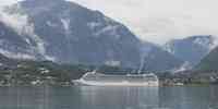 

Hvit cruiseskip i en fjord med skydekkede fjell i bakgrunnen.