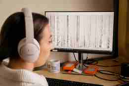 Kvinne med høretelefoner lytter til lydutslag på PC-en 