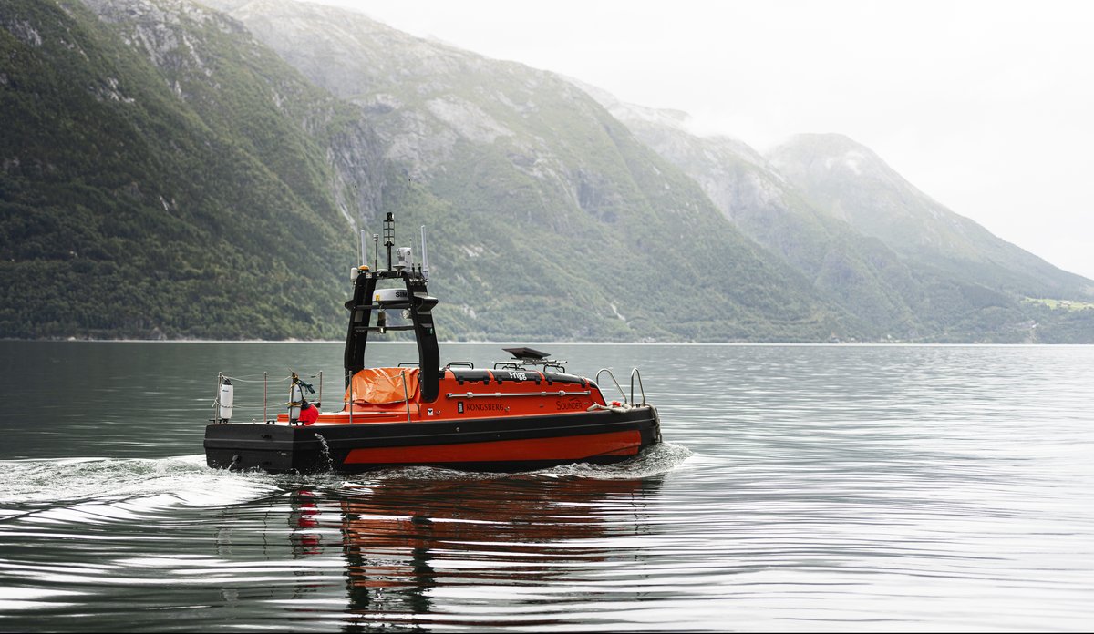 
Oransje fartøy ute på fjord med bratte fjellsider i bakgrunnen