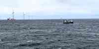 

Fiskebåt passerer vindturbiner i hav med skummende bølger 