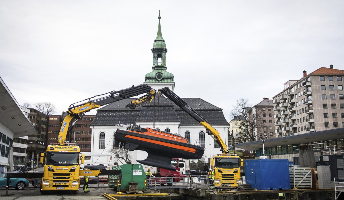 
To kranbiler står på en kai, der de heiser en usv ned i fjorden.