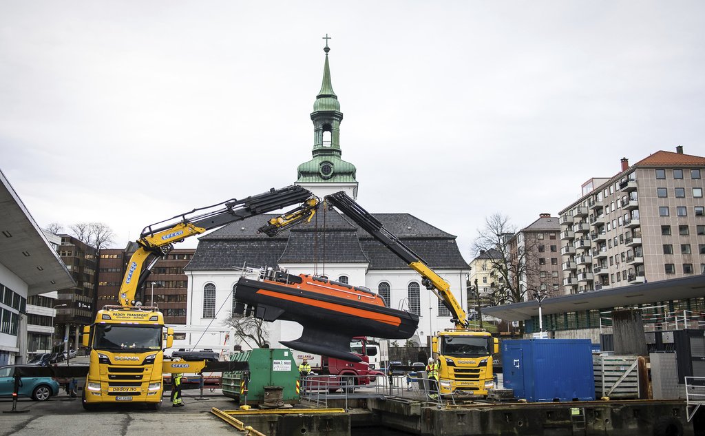 To kranbiler står på en kai, der de heiser en usv ned i fjorden.