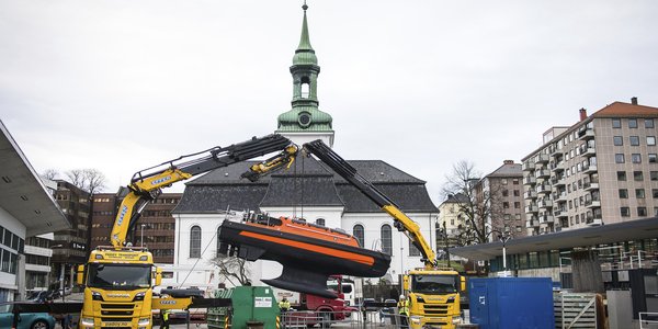 

To kranbiler står på en kai, der de heiser en usv ned i fjorden.