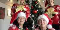 

Fire kvinner med røde julegensere og nisseluer og et juletre i bakgrunnen.