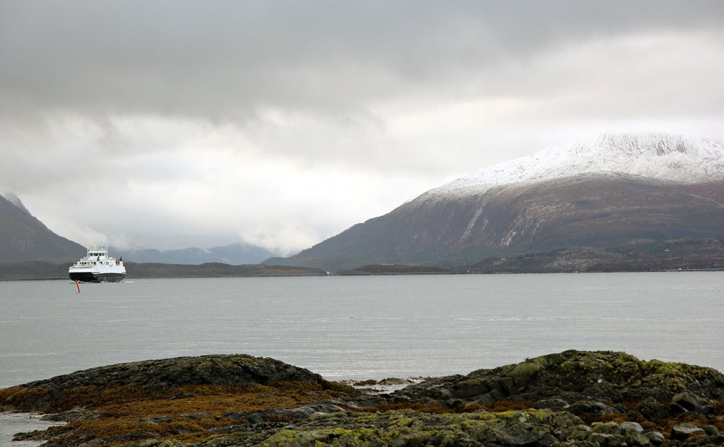 Fjord med ferje og snøkledde fjell og grå skyer i bakgrunnen