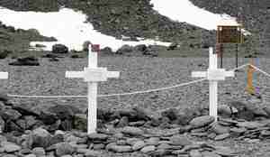 to hvite kors med norske flagg og navn på, stående på steinstrand 
