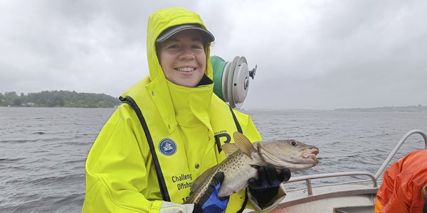 

Kvinne med gul regnjakke i båt holder en torsk.