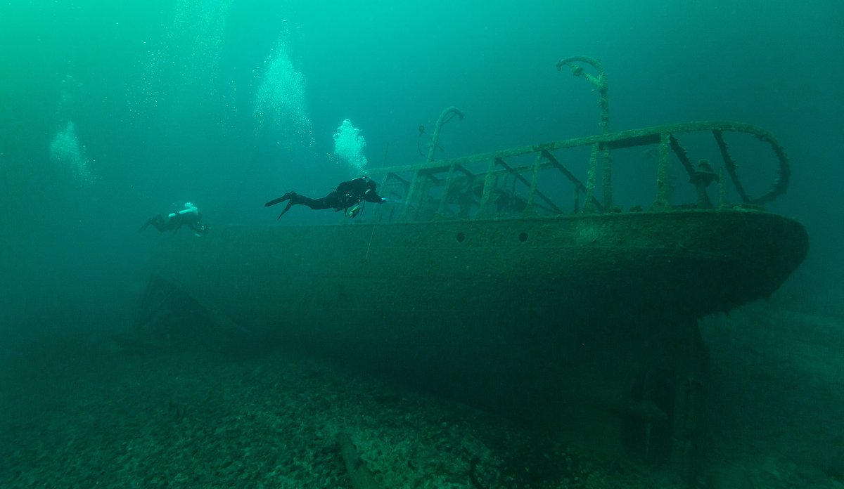 To dykkere undersøker et skipsvrak som ligger på havbunnen.