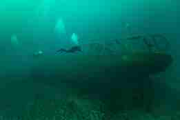 To dykkere undersøker et skipsvrak som ligger på havbunnen.