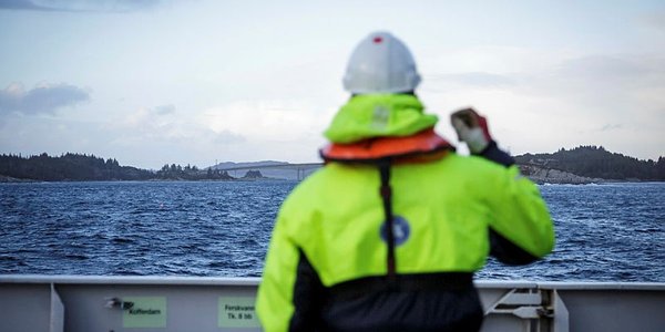 

person i arbeidstøy står ved skutesiden og ser utover sjøen