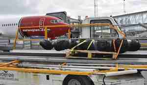 Transportbånd som brukes til å hente bagasje ut av fly med innpakket hai på, står parkert ved siden av et Norwegian-fly.