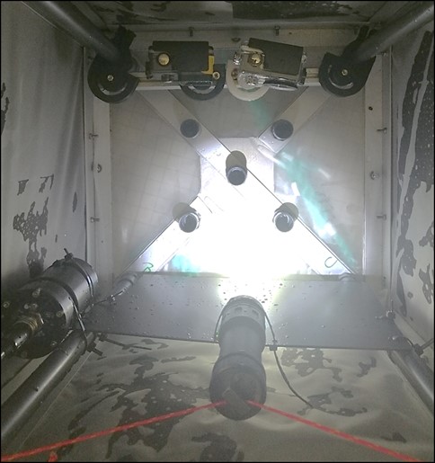 Picture is a picture showing the inside of the cage, where one can see the two cameras positioned along one of the side walls and the light hanging along the opposite side wall, the walls are of fine plankton mash. The frame is in steel. 