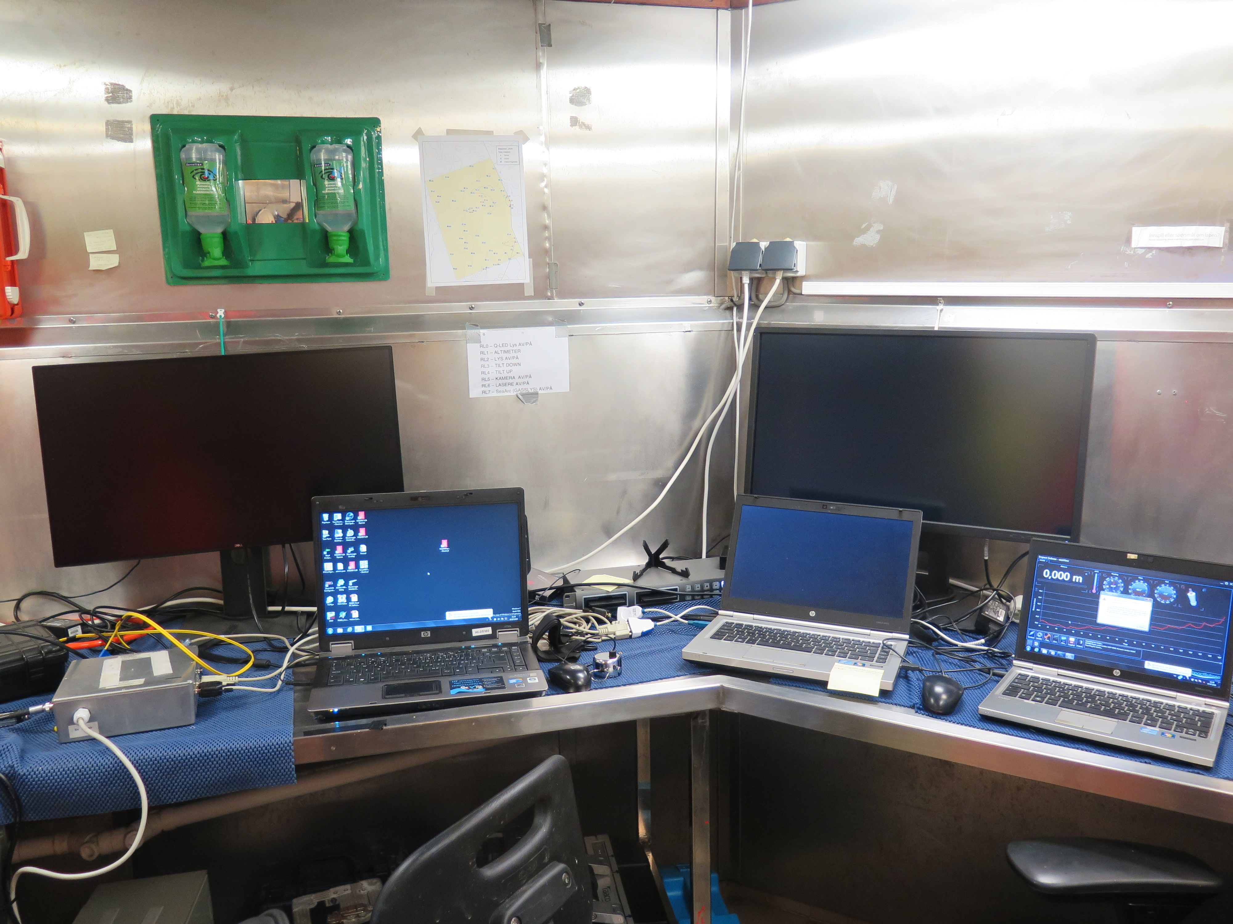 Bildet viser teknisk utstyr som benyttes ved filming med videosleden. Tre PCer er oppstilt på benken, og store skjermer står bak. 