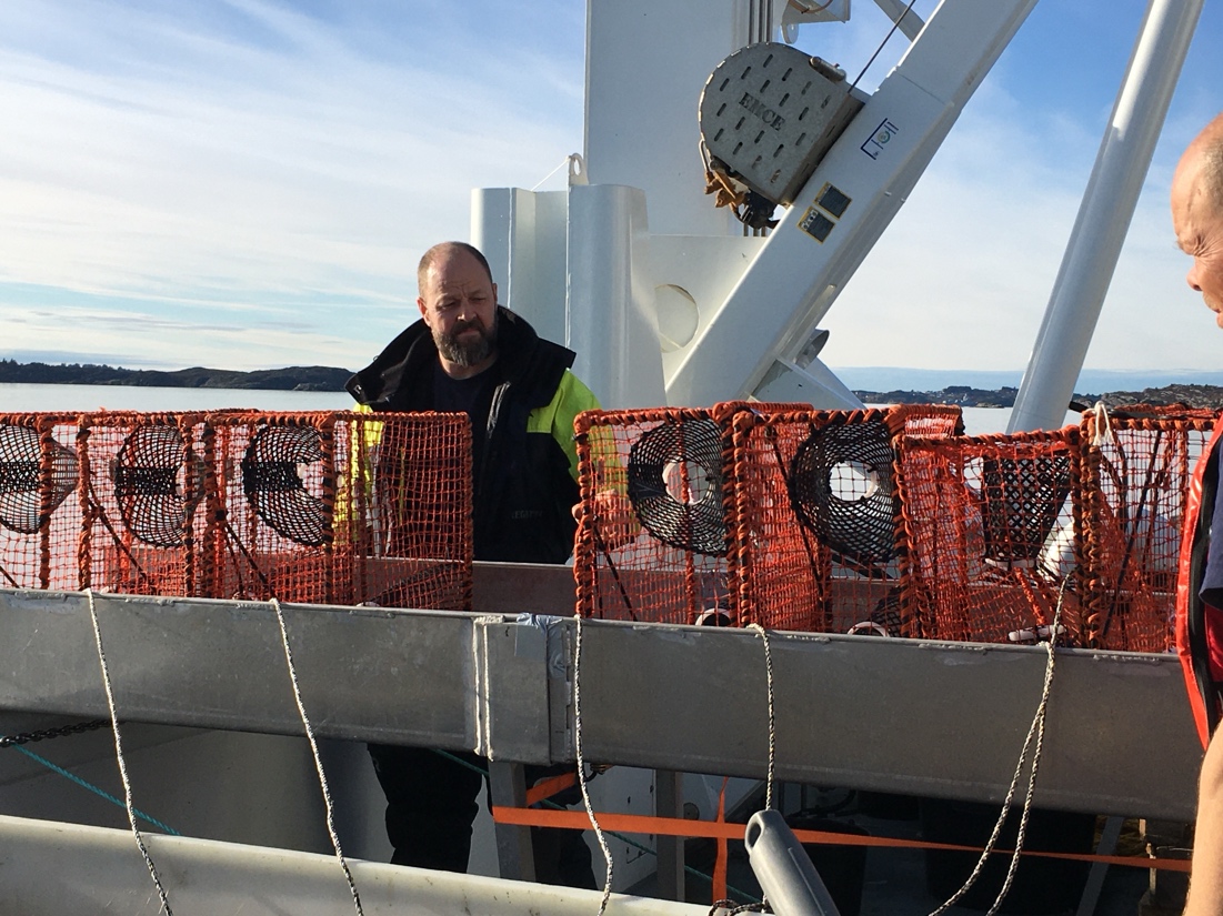 A picture shows seven Nephrops pots lined on a metal ramp. Two cruise participants are visible in the picture.