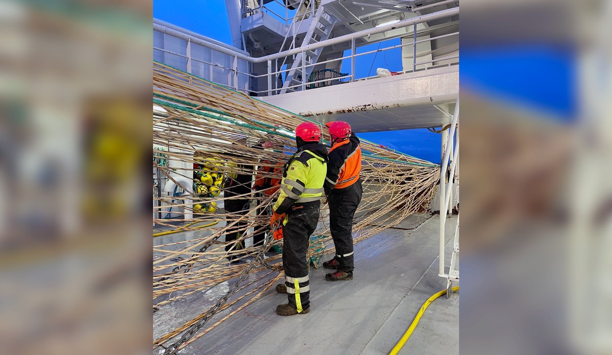To personer i kjeledress baler med en trål på dekk på båt.