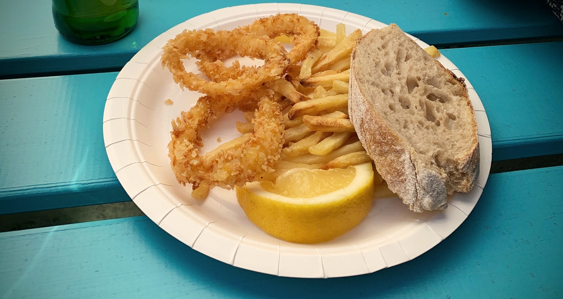 foto av en papptallerken med friterte, pankonerte ringer av blekksprut, pommes frites, brød og en sitronskive