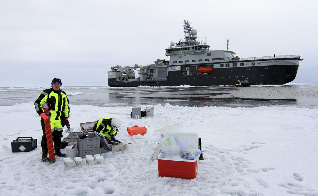 Forsker Melissa Chierici står på et isflak og tar prøver. Prøveutstyr ligger på isen, og på havet bak henne ser man forskningsskipet. 