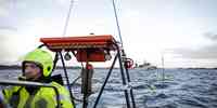 

Forskere i arbeidstøy på båt senker utstyr i fjorden.