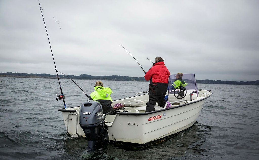 Foto av en småbåt med påhengsmotor. Tre personer er oppi med ryggen til. De holder hver sin fiskestang.