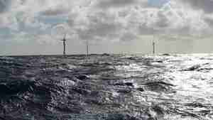tre vindturbiner i grå bølger ute på havet 