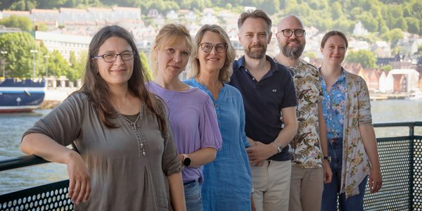 

Seks forskarar står ute på ein veranda, med Vågen og Bryggen i Bergen i bakgrunnen.